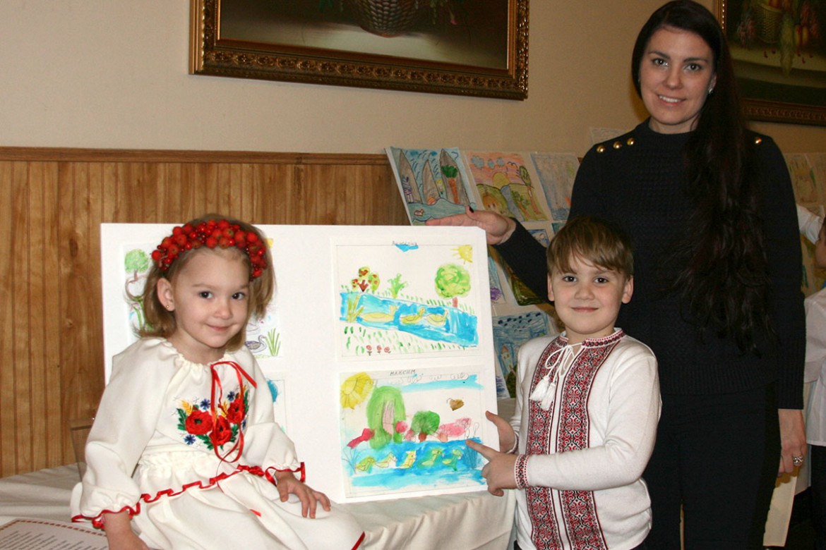 Максим Муртазин показує свій малюнок на виставці мамі Марті і сестрі Софійці.